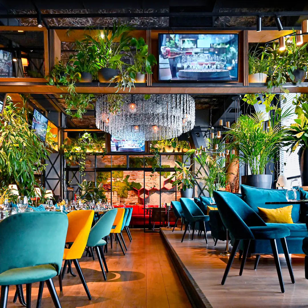 Modern restaurant interior with vibrant chairs, lush plants, and elegant lighting.